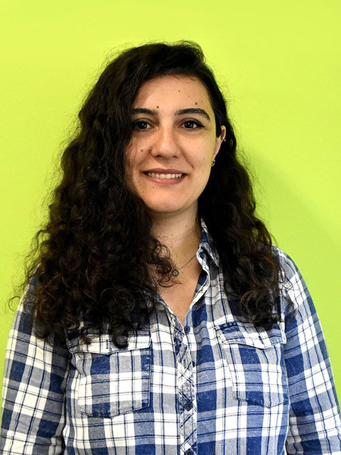 Doctoral Researcher Ezgi Aral wearing a checked black and white shirt in front of a green background